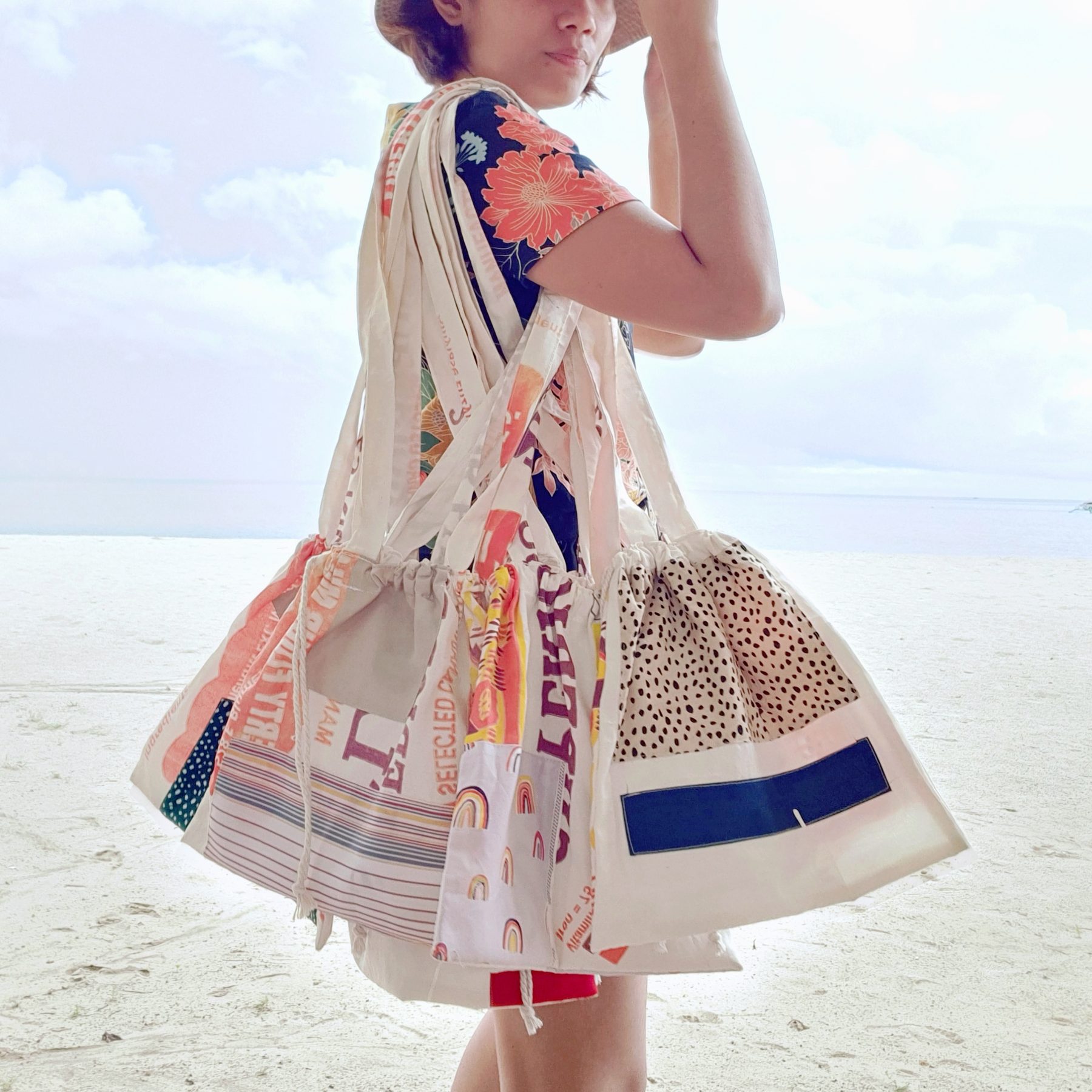 A patchwork katsa beach tote made of upcycled flour sacks, carried on a bright shoreline