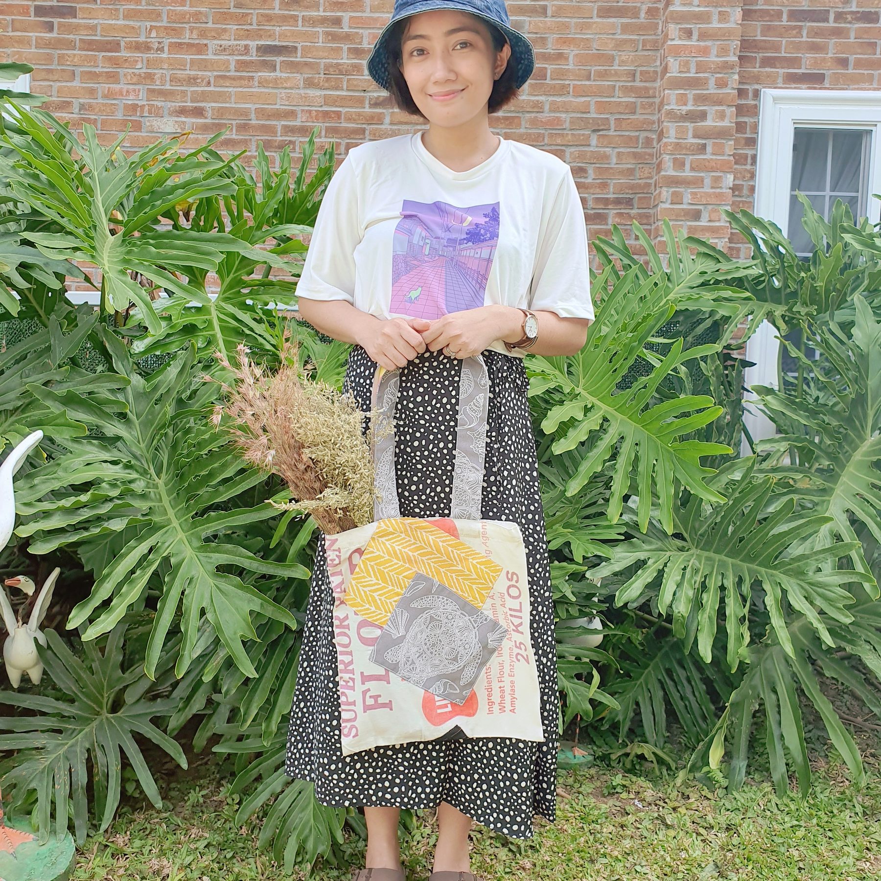 Woman holding an upcycled flour-sack tote in a leafy garden