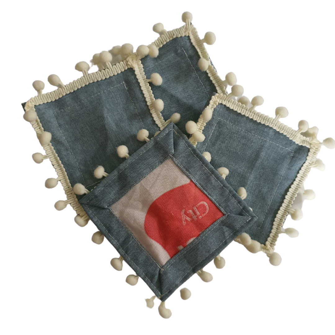 The Ashley Coasters: Set of four fabric coasters in light denim with pompom trim.